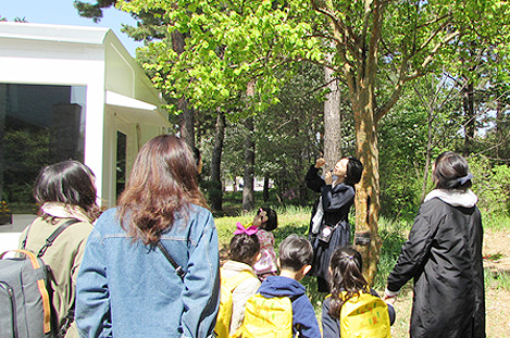 프로그램 해설사가 5명의 아이들과 3명의 학부모에게 나무를 바라보며 설명하고 있다