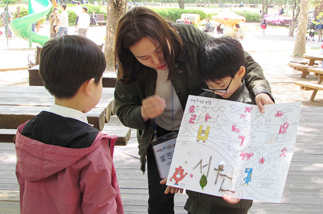 한 아이와 학부모가 맞은편의 아이에게 자신이 도화지에 그린 가족공원 전경을 설명하고 있다