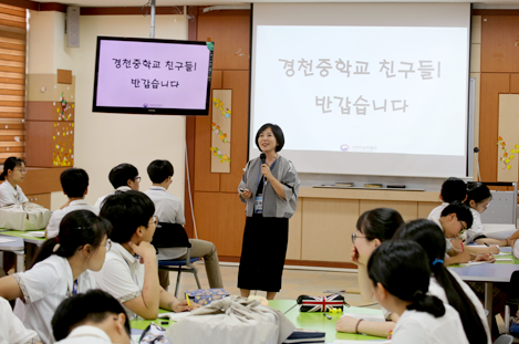 ‘경천중학교 친구들! 반갑습니다’라고 적힌 화면 앞으로 오재은 강사가 마이크를 들고 학생들과 인사하고 있다. 13명의 학생들이 오재은 강사의 모습을 자리에 앉아 바라본다.