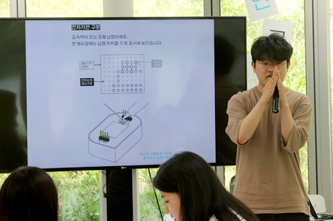 남성 강사가 대형 모니터 앞에 서 마이크를 쥔 채 세종전자얼굴을 만드는 방법에 대해 설명하고 있다.