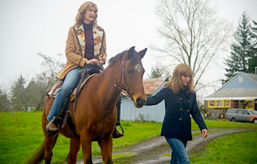 영화 <와일드>의 스크린샷. 중년의 여성이 갈색 말 위에 올라타 있으며, 다른 젊은 여성은 말의 고삐를 잡아 이끌고 있다.