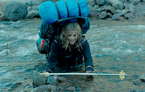 한 여성이 침낭까지 둘러맨 여행용 배낭을 짊어지고 등산 스틱을 손에 쥔 채 강물을 건너고 있다.