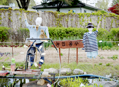 ‘농업용수’라 적힌 나무팻말아래 시냇물이 흐르고 두 개의 허수아비가 자리를 지키고 있다.