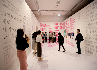 전시장 내부를 둘러보는 10여 명의 기자들과 이들에게 전시에 대해 마이크를 들고 안내하는 김미미 학예연구사.