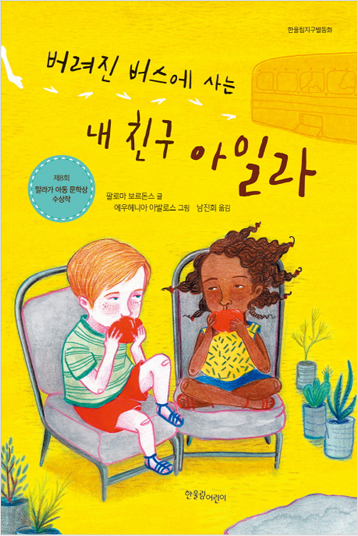 도서 《버려진 버스에 사는 내 친구 아일라》의 표지. 백인 소년과 흑인 소녀가 의자에 앉아 빨간 사과를 양손에 쥔채 먹고 있다. 