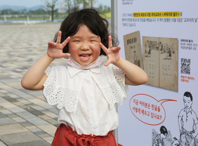 입간판 앞에서 양팔을 들어 포즈를 취한 여자 어린아이.