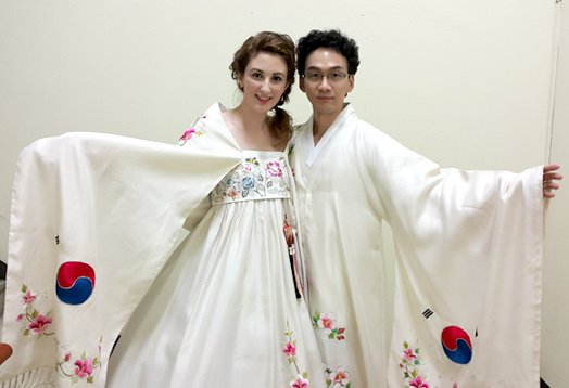 크리스티나와 김현준 부부가 태극기와 무궁화가 수놓인 새하얀 한복을 입고 양 팔을 펼쳐보이며 포즈를 취하고 있다.