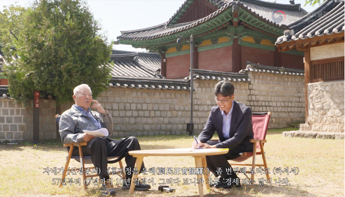 체크무늬 셔츠를 입고 회색 바람막이를 입은 강신항 교수와 네이비 정장을 차려입은 면담자와 나무 테이블 앞의 의자에 앉아 대화하고 있다. 그들은 옛 기와 건물과 담벼락 앞의 잔디밭에서 이야기하고 있다. 
“자네가 (신경준의) 《훈민정음 운해》 좀 번역해 보라고 (하셔서) 57년부터 67년까지 10년 걸렸어. 그러다 보니까 자꾸 ‘경세’라는 말이 나와.”