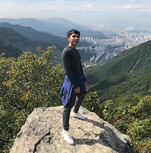 
한국의 어떤 산 바위 위에 오른 제레미. 바위 뒤로 산의 풍경과 도심이 조그맣게 보인다. 흰 운동화에 검정 트레이닝복을 입고 있다.