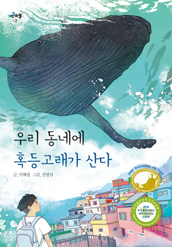 도서 《우리 동네에 혹등고래가 산다》의 표지. 색색의 건물이 자리한 동네가 삽화 우측 하단에 그려져 있고 왼쪽에는 짧은 머리의 소년이 백팩을 맨 체 어딘가를 응시하고 있다. 하늘이 있어야 할 곳은 바다로 표현되어 있는데, 커다란 혹등고래가 하늘바다를 누비고 주변으로 물고기들이 잔뜩 그려져 있다.