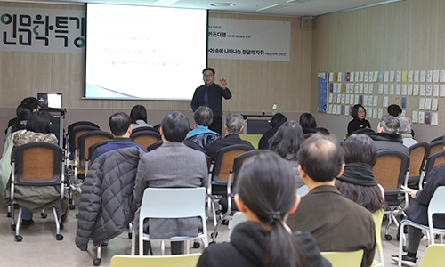 인문학특강 플랜카드가 걸린 강의실에서 한 남자 강사가 강연하고 있다. 강의실은 의자로 가득 채워져 있고 20여 명의 관객이 강사의 말을 경청하고 있다.