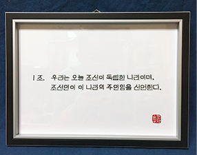 진형준 작가의 블록 작품 <브릭으로 쓰는 독립선언서> 1조. ‘1조. 우리는 오늘 조선이 독립한 나라이며, 조선인이 이 나라의 주인임을 선언한다.’이 인쇄물로 출력돼 액자에 전시되어 있다. 인쇄물 오른쪽 하단에는 붉은색으로 진형준 작가의 인장이 찍혀있다.