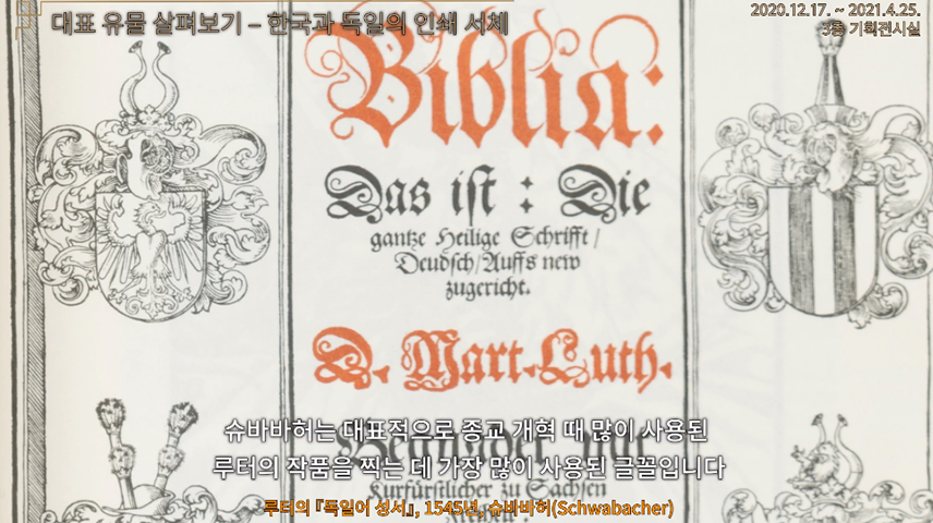 “기획특별전 ‘문자 혁명-한국과 독일의 문자 이야기’_대표 유물 살펴보기Ⅲ” 영상 캡처. 영상 하단에 자막으로 ‘슈바바허는 대표적으로 종교 개혁 때 많이 사용된 루터의 작품을 찍는 데 가장 많이 사용된 글꼴입니다’라고 적혀있다. 화면에는 루터의 독일어 성서의 일부분이 확대되어 있다. 가운데는 주황색과 검은색의 독일 문자가 크게 적혀있으며, 양옆으로는 화려한 문양의 그림들이 그려져 있다.
