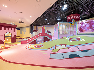한글놀이터 전시장 전경. 놀이터 공간은 전체적으로 분홍빛이 돌며, 바닥엔 분홍색, 노란색, 하늘색, 연두색이 섞여 있다. 아이들이 놀 수 있는 미끄럼틀 및 여러 놀이기구와 벽면에는 영상 스크린이 설치되어 있다.