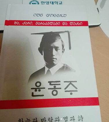 윤동주 시인과 관련된 내용이 담긴 책 표지. 하얀색 바탕에 학사모를 쓴 윤동주 시인의 초상화가 흑백으로 새겨져 있다. 그 밑에는 커다랗게 ‘윤동주’라고 적혀있으며, 초상화를 기준으로 위, 아래에 빨간색 줄이 그어져 있다. 책 하단에는 ‘하늘과 바람과 별고 詩’라고 적혀있다. 상단에는 조지아 국가의 글자가 적혀있다.