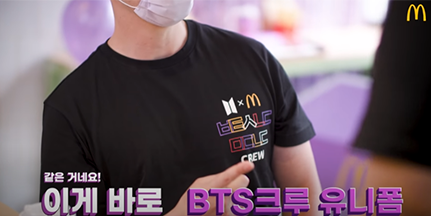 한국 맥도날드 유튜브 영상 캡처. 한 남성이 맥도날드와 방탄소년단이 협업한 ‘BTS크루 유니폼’을 입고 있다. 유니폼은 검은색이며, 왼쪽 가슴 쪽에 맥도날드와 방탄소년단의 마크가 그려져 있고, 자음 ‘ㅂㅌㅅㄴㄷ’과 ‘ㅁㄷㄴㄷ’가 적혀있다.