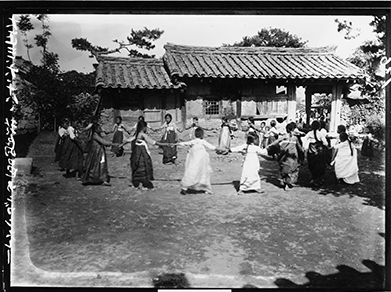 강강술래를 하는 모습을 찍은 흑백 사진이다. 오래되어 보이는 기와집 앞마당에서 한복을 입은 여성들이 동그랗게 모여 손을 잡은 채 강강술래 놀이를 하고 있다.