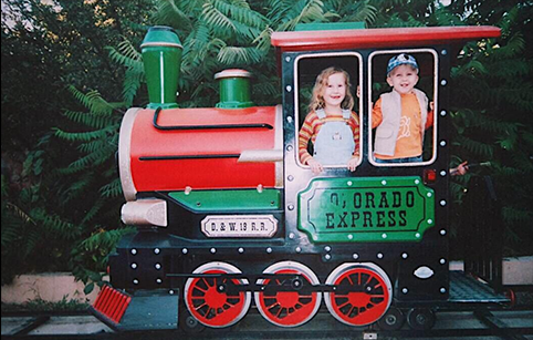 어린이용 기차에 어린 알리사와 남동생이 타고 있다. 기차는 녹색과 빨간색으로 꾸며져 있다. 알리사와 남동생은 각각 기차 창문 앞에 서서 카메라를 향해 개구지게 웃고 있다. 기차 뒤로는 무성한 풀숲이다.