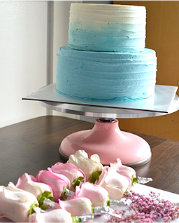 탁자 위에 케이크와 꽃이 올려져 있다. 꽃은 흰색과 분홍색이 은은하게 섞인 장미꽃으로 가지런하게 나열되어 있다. 케이크는 2단 케이크로 흰색과 하늘색이 그러데이션 되어있다.