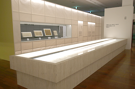 기획전시실 내부 사진으로, 흰색의 긴 전시 진열대 안에 전시 유물들이 놓여있다. 벽면에도 한글과 관련된 전시 유물이 놓여있다.