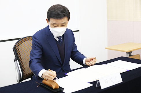 허성곤 김해시장이 업무협약서에 서명하고 있다. 그는 남색 재킷과 남색 넥타이, 흰색 마스크를 착용하고 있다.