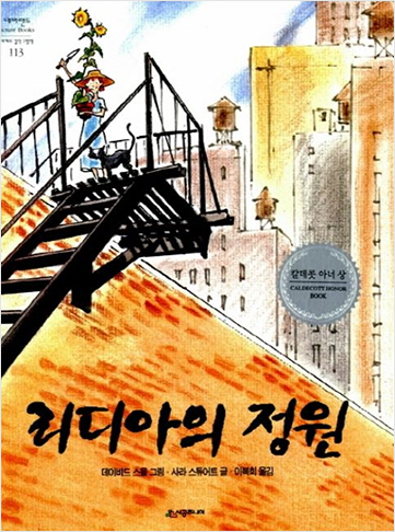 도서 『리디아의 정원』의 표지. 왼쪽에 건물로 올라가는 검은 철제 계단이 보이고 계단 위에 여자아이가 서 있다. 아이는 밀짚모자를 쓰고, 파란색 반팔 원피스를 입고 있다. 품에는 머리 위로 높게 치솟은 해바라기 화분을 안고, 모종삽을 치켜들고 있다. 아이 옆에는 검은 고양이가 함께 서 있다. 아이의 뒤로 빽빽하게 들어선 높은 빌딩들이 보인다.