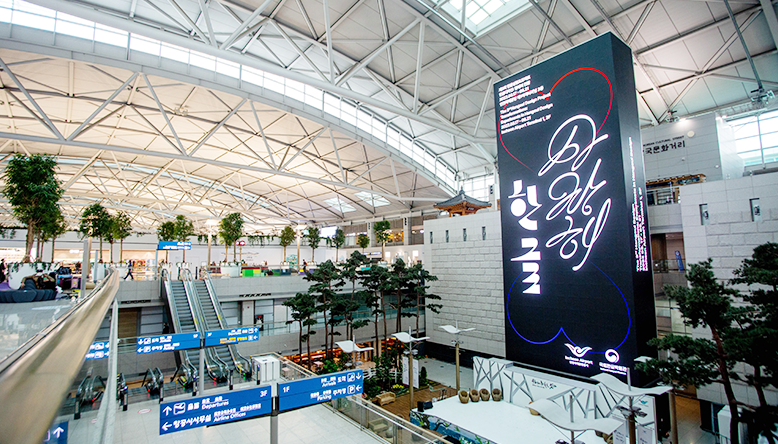 인천공항 내부 모습으로 넓게 펼쳐진 공간 안에 세워진 대형 미디어 타워가 보인다. 미디어 타워는 검은색의 커다란 직사각형 구조물로 ‘한글 사랑해’가 적혀있다.