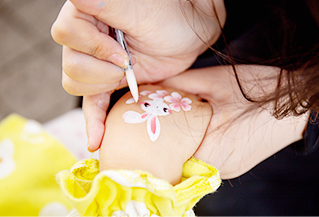 한 여성이 어린아이의 손등에 붓으로 하얀 토끼와 꽃을 그려주고 있다.
