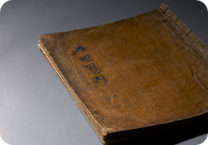 『사민필지』가 비스듬히 놓여있다. 책은 심하게 낡아 있으며 표지에 ‘사민필지’라고 세로쓰기 되어있다.