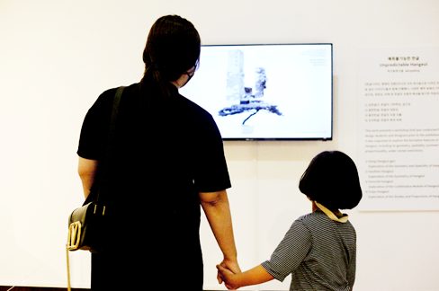 엄마와 아이가 손을 잡고 나란히 서서 전시장에 설치된 멀티미디어 전시작품을 관람하고 있다. 엄마와 아이는 뒷모습만 보인다.