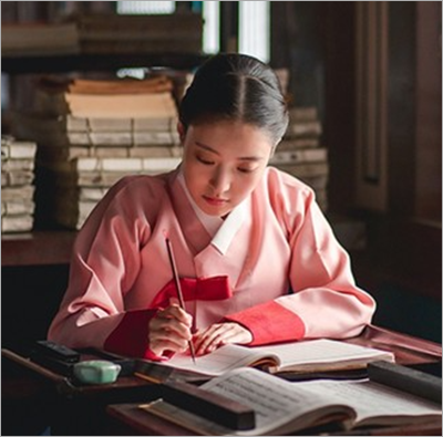 어둑한 책방에 옛 고서들이 잔뜩 쌓여 있다. 분홍색 저고리를 입은 조선 시대 여성이 얇은 붓을 들고 책을 필사하고 있다. 곁에는 먹과 문진이 함께 놓여있다.