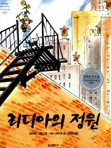 도서 『리디아의 정원』의 표지. 왼쪽에 건물로 올라가는 검은 철제 계단이 보이고 계단 위에 여자아이가 서 있다. 아이는 밀짚모자를 쓰고, 파란색 반팔 원피스를 입고 있다. 품에는 머리 위로 높게 치솟은 해바라기 화분을 안고, 모종삽을 치켜들고 있다. 아이 옆에는 검은 고양이가 함께 서 있다. 아이의 뒤로 빽빽하게 들어선 높은 빌딩들이 보인다.