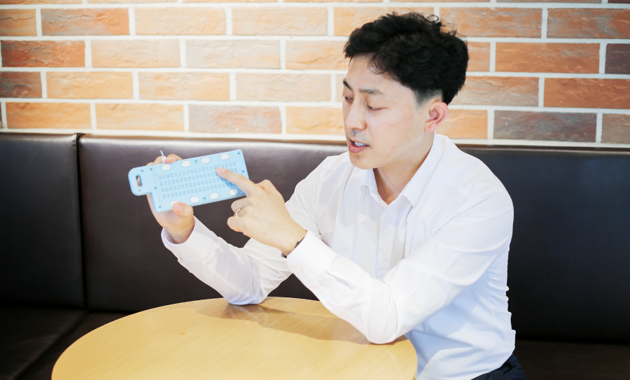쇼파에 앉은 김상언 대표가 버사 슬레이트를 들고 손가락으로 가리킨 채 무언가를 말하고 있다.
