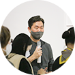 작품 곁에서 강사가 하얀 마이크를 든 채 무언가 설명하고 있다. 그는 검은색 마스크를 착용했다. 작품 앞에서는 사람들이 설명을 들으며 무언가 받아적고 있다.
