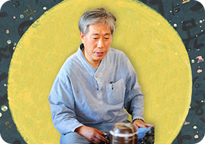 회색 개량 한복을 입은 이호신 화가가 앉아있다. 그의 작품 <한글은 세상의 어둠을 밝히는 별>이 배경으로 있는데, 노란색 달 주위로 짙은 파란색 배경에 한글과 별이 군데군데 그려져 있다.