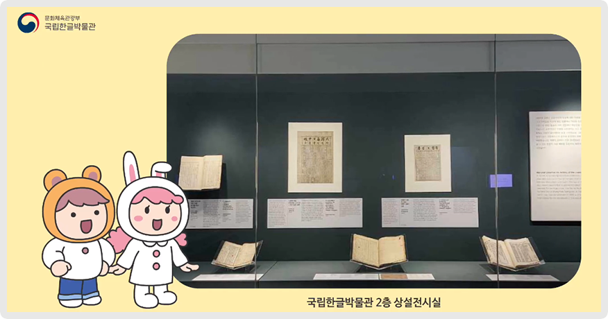 노란색 배경 속에 국립한글박물관 2층 상설전시실에 전시된 「독립신문」 사진이 있다. 사진 왼쪽엔 어린이 두 명이 사진을 바라보고 있는 그림이 그려져 있다.