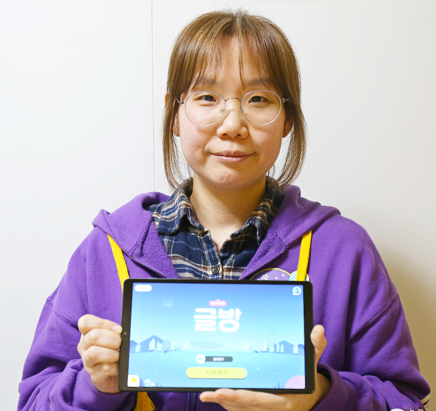 보라색 옷을 입은 에누마코리아의 김은파 기획자가 태블릿을 들고 정면을 바라보고 있다.
