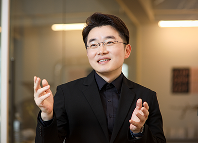 반갑습니다 기사 사진. 검은색 정장을 입고 안경을 쓴 김동호 수어 통역사가 양손을 들고 왼쪽을 바라보고 있다.