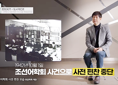 한박튜브 기사 사진. 2023년 국립한글박물관 <화요 한글문화 강좌> 제2회차 강연, 성균관대학교 동아시아역사연구소 정재환 책임연구원의 ‘벤또(X)?!→도시락(O)!! 해방과 함께한 우리말 독립운동’ 영상 장면이다. 정재환 책임연구원이 두 손을 모으고 앉아 이야기하고 있고, 왼쪽엔 여러 사람이 빙 둘러앉아 일하고 있는 ‘조선어학회’ 옛날 사진이 있다.