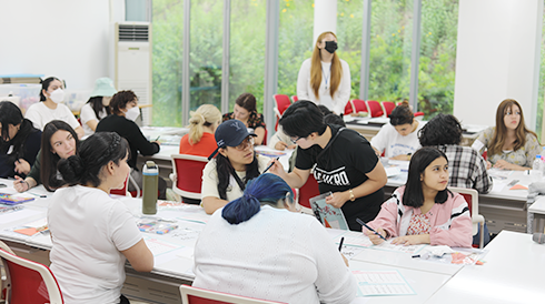 ‘손으로 꽃피우는 한글’ 교육 현장 사진이다. 외국인 수강생들이 한글 캘리그래피 체험을 하며 오른쪽을 쳐다보고 있다. 