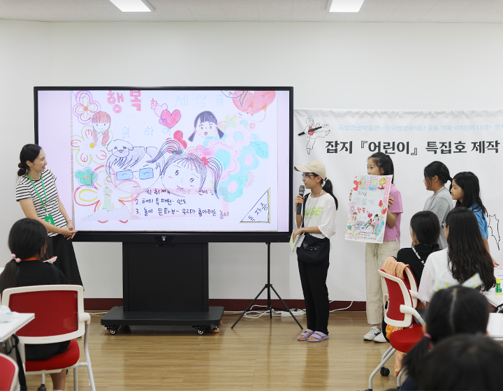 박물관은 지금 기사 사진. 기획 전시 <어린이 나라>와 연계하여 국립한글박물관과 한국방정환재단이 공동으로 기획한 ‘잡지 『어린이』 특집호 만들기’ 현장 사진이다. 마이크를 든 한 여자 어린이가 화면을 띄워놓고 무언가를 발표하고 있다. 화면 속엔 어린이 형상의 얼굴 그림이 여러 개 그려져 있다. 