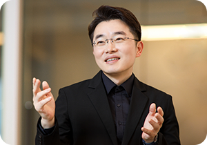 검은색 정장을 입고 안경을 쓴 김동호 수어 통역사가 양손을 들고 왼쪽을 바라보고 있다.