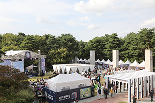 2023년 한글날 국립한글박물관 전경 사진이다. ‘2023 한글주간’ 행사가 펼쳐지고 있다. 정면엔 큰 부스가 설치돼 있으며, 들판 위에 설치된 무대에선 공연이 진행 중이다. 사람들이 빼곡하게 앉거나 서 공연을 보고 있으며, 오른쪽 옆엔 작은 부스들이 설치돼 있다.
