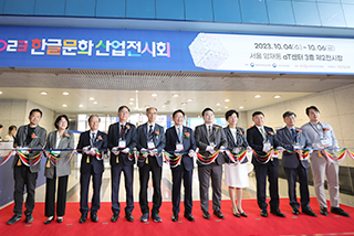 <2023 한글문화산업전시회> 현장 사진이다. 관계자들이 입구 앞에서 커팅식을 진행하고 있다.