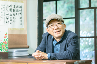 남색 정장과 파란색 셔츠를 입은 나태주 시인이 의자에 앉아 책상에 두 손을 모아 올리고 정면을 응시하고 있다. 나태주 시인은 안경과 모자를 썼으며 환하게 웃고 있다. 나태주 시인의 왼쪽엔 나태주 시인의 대표작인 「풀꽃」의 시구가 새겨진 흰색 상자 모양에 빨간 꽃들과 풀잎이 그려져 있다. 그 뒤엔 흰색 종이들이 쌓여 있으며, 그 위로는 「풀꽃」의 시구가 황토색 두루마기 형식의 종이에 담겨있다.