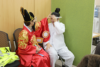 특수학급 학생들을 대상으로 한 한글문화 체험 교육 <세종의 친구, 한글 지킴이>의 시범 현장 사진이다. 임금님 복장을 한 왼쪽 사람이 흰색 옛 복장을 한 사람의 머리띠를 만지고 있다.