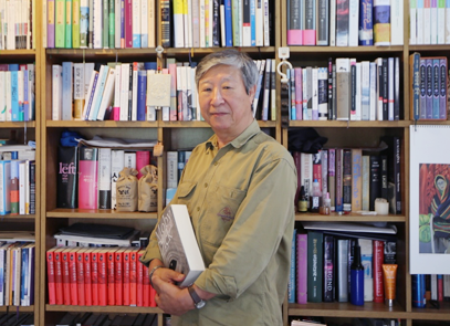 반갑습니다 기사 사진. 김석희 번역가가 양손을 모아 도서 『모비 딕』을 들고 측면으로 비스듬히 서 정면을 바라보고 있다. 그의 뒤엔 책들이 빼곡하게 꽂혀있는 책장들로 꽉 차 있다.