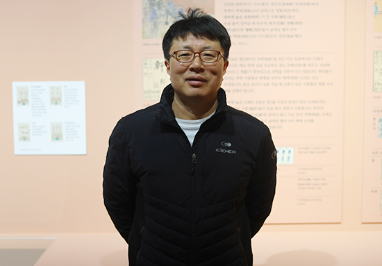 한글 노래 『한양가』를 중심 주제로 한 기획특별전 <서울 구경 가자스라, 한양가> 전시 현장 미니 인터뷰 사진이다. 한 남성이 손을 뒤로 모은 채로 서서 정면을 바라보고 있다.