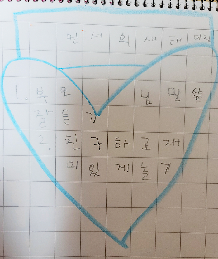 글씨 연습용 공책에 ‘민서의 새해 다짐, 1. 부모님 말씀 잘 듣기, 2. 친구하고 재미있게 놀기’라고 적혀있고, 하늘색으로 큰 하트와 네모가 그려져 있다.