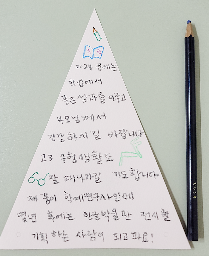 삼각형 모양의 종이에 ‘2024년에는 학업에서 좋은 성과를 이루고 부모님께서 건강하시길 바랍니다. 고3 수험생활도 잘 해나가길 기도합니다. 몇 년 후에는 한글박물관 전시를 기획하는 사람이 되고파요!’라고 적혀있다.